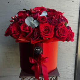 Red roses arranged in a round red hat box with a ribbon