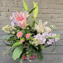 Pink and white lilies with lavender flowers in a pink container