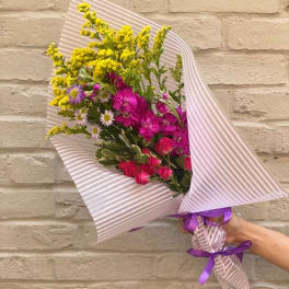 Hand-tied bouquet of pink and yellow flowers wrapped in striped paper