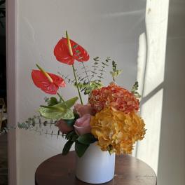 Arrangement of red anthuriums, hydrangeas, and pink roses in a white vase