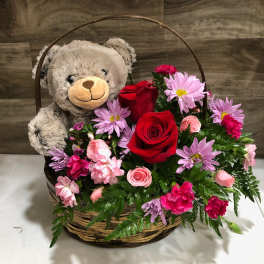 Teddy bear in a basket with red roses and pink flowers