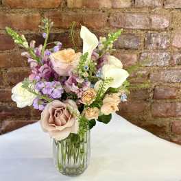Pastel bouquet of roses, calla lilies, and purple blooms in a glass vase