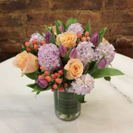 Bouquet of peach roses, lavender blooms, and purple tulips in a glass vase