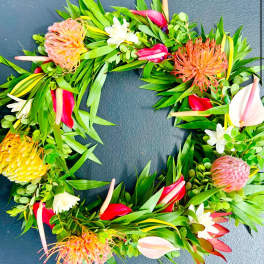 Tropical wreath of green foliage with protea and red, yellow, and white flowers on a dark surface