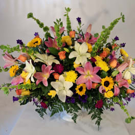 Large mixed bouquet with lilies, roses, sunflowers, and purple accents in a clear vase