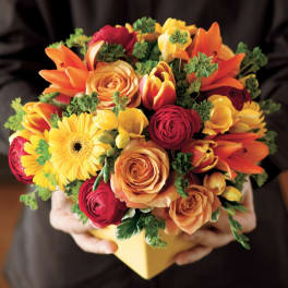 Mixed bouquet of orange, yellow, and red flowers in a yellow box