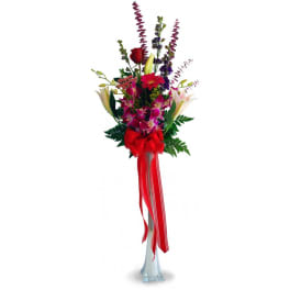 Tall bouquet of mixed flowers in a clear vase with a red ribbon