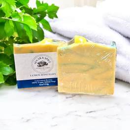 Two wrapped bars of lemon rosemary soap beside green leaves and towels