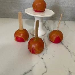 Four caramel apples on sticks, arranged around a small white pedestal stand