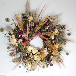 Dried floral wreath with pink and cream blooms on a white wall