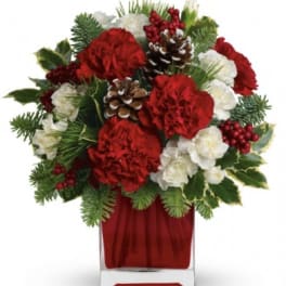 Red and white floral arrangement in a clear vase with pinecones and berries