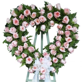 Heart-shaped wreath of pale pink roses with a white ribbon bow