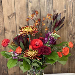 Mixed bouquet in a clear vase with orange, red, and purple blooms