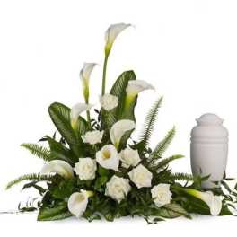 White calla lilies and roses arranged beside a white urn