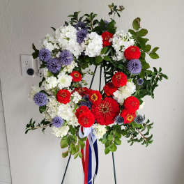 Circular floral wreath on an easel with red, white, and purple flowers