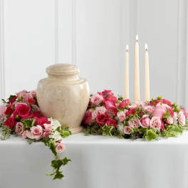 Pink rose floral centerpiece with a beige urn and three taper candles