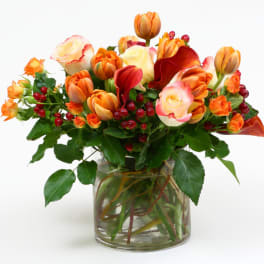 Orange and cream tulips with red berries in a glass vase