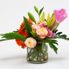 Mixed bouquet of pink tulips, roses, and orange flowers in a glass vase