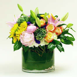 Mixed bouquet of pink lilies, yellow daisies, and roses in a glass vase