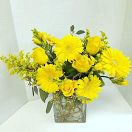 Yellow roses and gerbera daisies in a square glass vase