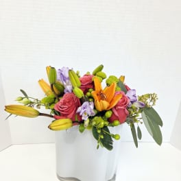 Mixed bouquet of pink roses, orange lilies, and purple flowers in a white vase