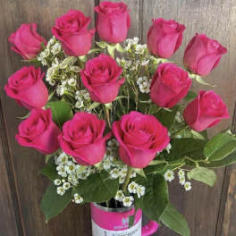 Hot pink roses arranged in a pink tumbler with small white filler flowers