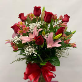 Bouquet of red roses and pink lilies in a glass vase with a red ribbon