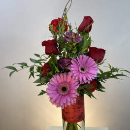 Tall bouquet of red roses and pink gerbera daisies in a glass vase