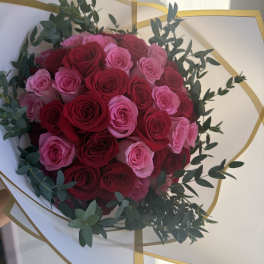 Round bouquet of red and pink roses wrapped in white paper with gold trim
