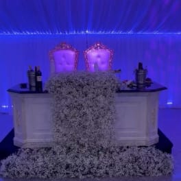 Large white floral arrangement draped over a white table in a blue-lit room