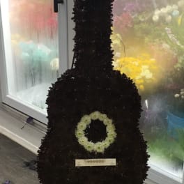 Large guitar-shaped floral arrangement made of dark flowers with pale accents.