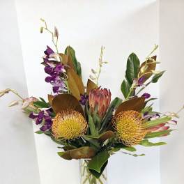 Tropical flower arrangement in a tall clear vase with purple orchids and yellow pincushion blooms
