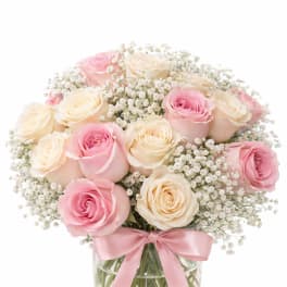 Pink and cream roses in a glass vase with a pink ribbon