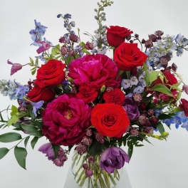 Bouquet of red roses and purple flowers in a clear glass vase