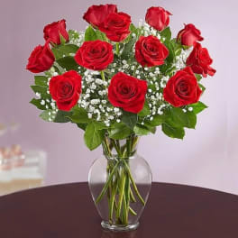 Arrangement of red roses with white filler flowers in a clear glass vase.