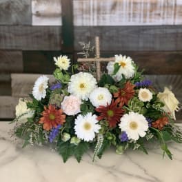 Low floral arrangement with white, orange, and pale pink blooms in a rope-wrapped cross base