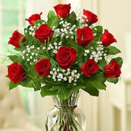 Red roses arranged in a clear glass vase with white filler flowers