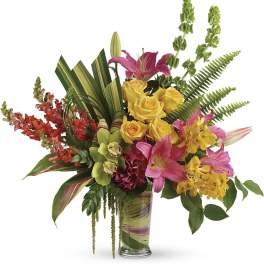 Mixed bouquet of pink lilies, yellow roses, and orchids in a glass vase