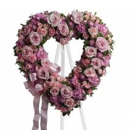Heart-shaped floral wreath of pink and purple flowers on an easel with ribbon