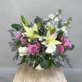 Bouquet of lilies, roses, and white filler flowers in a white vase