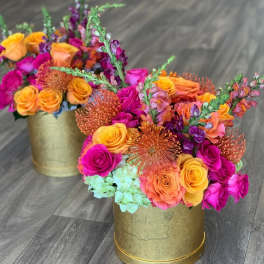 Two colorful floral arrangements in gold round containers