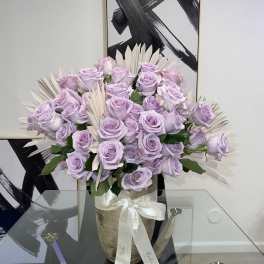 Lavender roses arranged in a vase with pale decorative leaves.