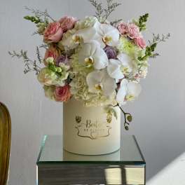 Pink roses and white orchids arranged in a cream hat box