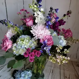 Mixed bouquet in a glass vase with pink roses, blue hydrangeas, and purple flowers