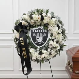 White floral funeral wreath with a Raiders emblem and black ribbon