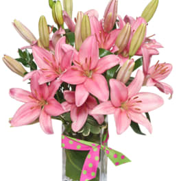 Pink lilies arranged in a clear glass vase with a polka-dot ribbon