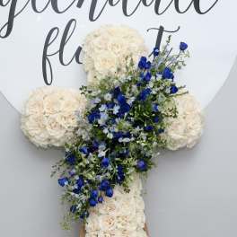 Cross-shaped floral arrangement with cream roses and blue flowers on an easel