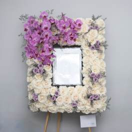 Floral easel frame of white roses, lavender roses, and pink orchids around a center opening