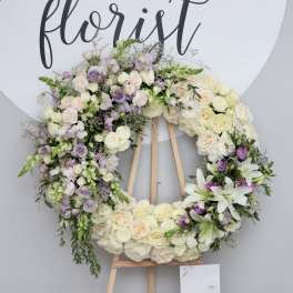Large floral wreath on a wooden easel with white, cream, and lavender flowers
