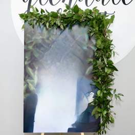 Green leafy garland draped over a large printed panel on an easel